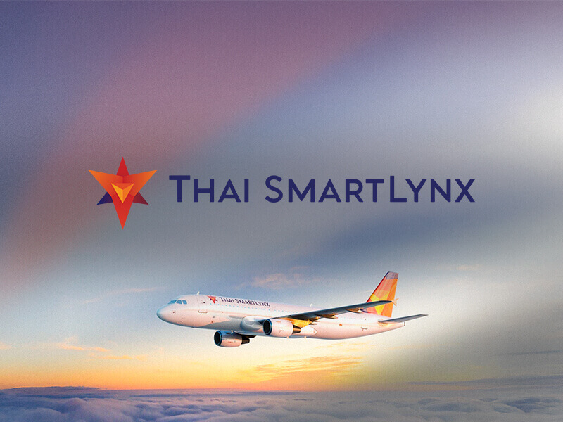 Thai SmartLynx aircraft flying above the clouds at sunset, with the airline logo displayed in the sky and warm light reflecting on the fuselage.