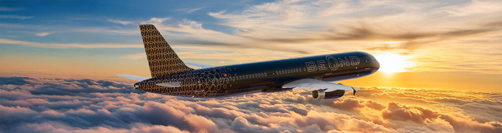 BeOnd aircraft cruising above a blanket of clouds at sunset, with golden light illuminating the fuselage and sky.