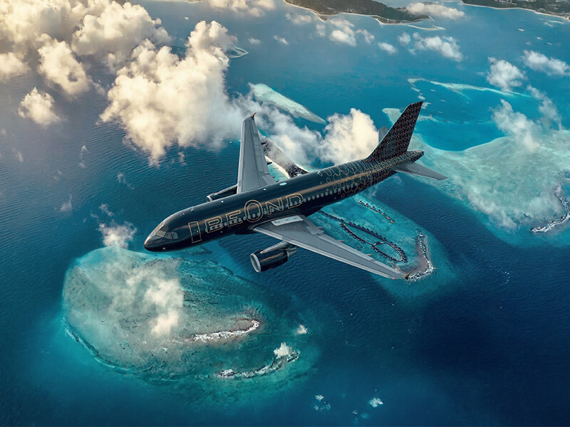 BeOnd aircraft flying above turquoise tropical islands and coral reefs, with scattered clouds over clear blue ocean.
